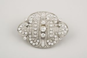 173 Broche Belle Époque realizado en platino, simétrico con líneas lobuladas caladas y grafiladas, en el centro destacan tres brillantes talla antigua, peso total aproximado 1,80 ct.00 173 Broche Belle Époque realizado en platino, simétrico con líneas lobuladas caladas y grafiladas, en el centro destacan tres brillantes talla antigua, peso total aproximado 1,80 ct.00